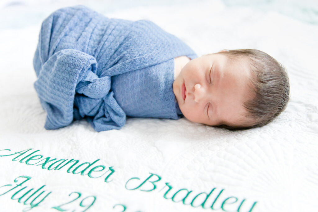 Baby lays swaddled next to his monogramed baby blanket during his lifestyle newborn session.