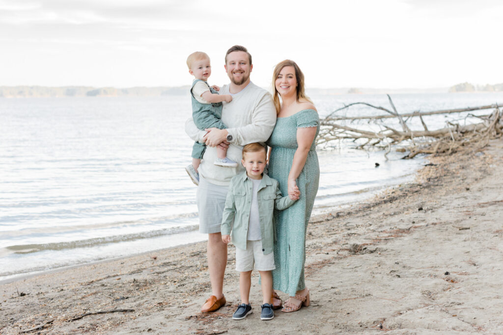 A family of 4 stand smiling at a beach near Buford, Georgia. They wear light green and white coordinating outfit choices.