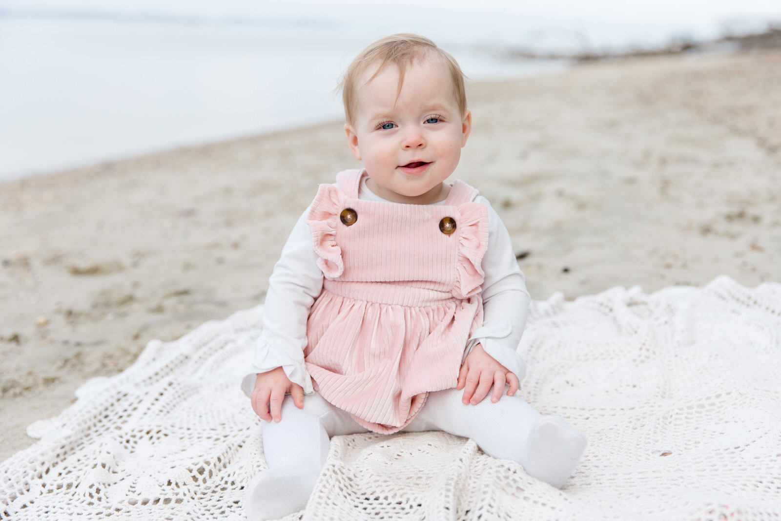 One year old daughter smiles on the beach at Lake Lanier and sits on sand