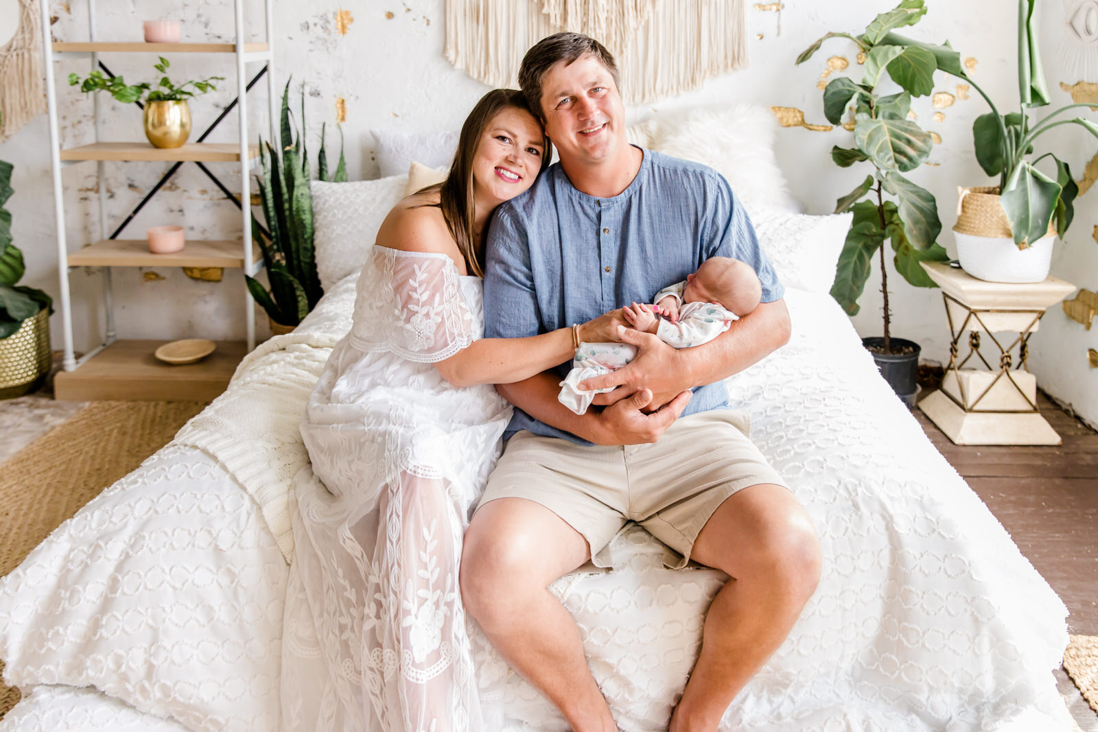 Mom and dad sit on the edge of a bed while holding newborn baby at lifestyle newborn session in Gwinnett County, Georgia