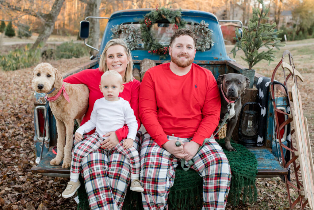 Family of 3 sit on the back of a decorated Christmas truck with their two dogs during a family session in Lawrenceville