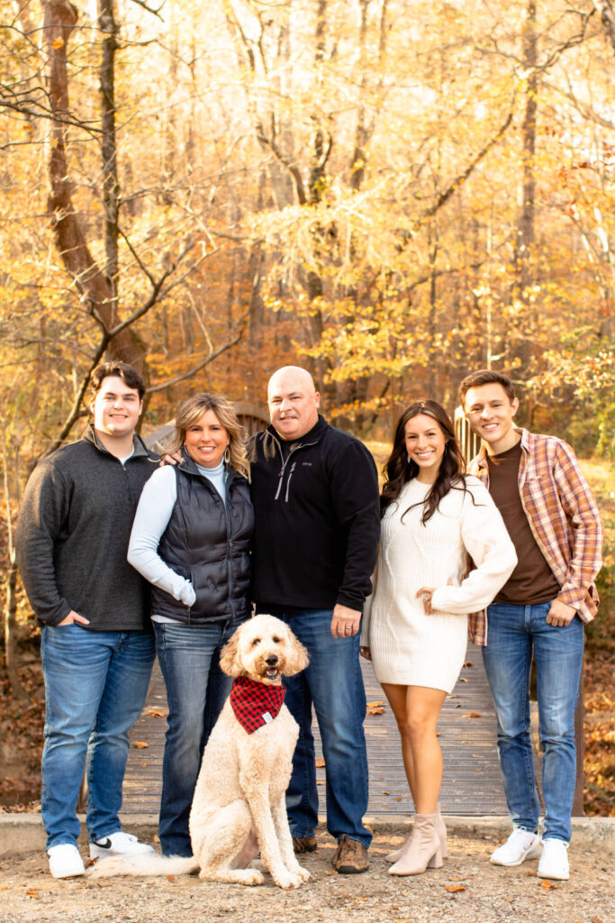 A family of 5 stand in front of a bridge with their dog during a family photo session