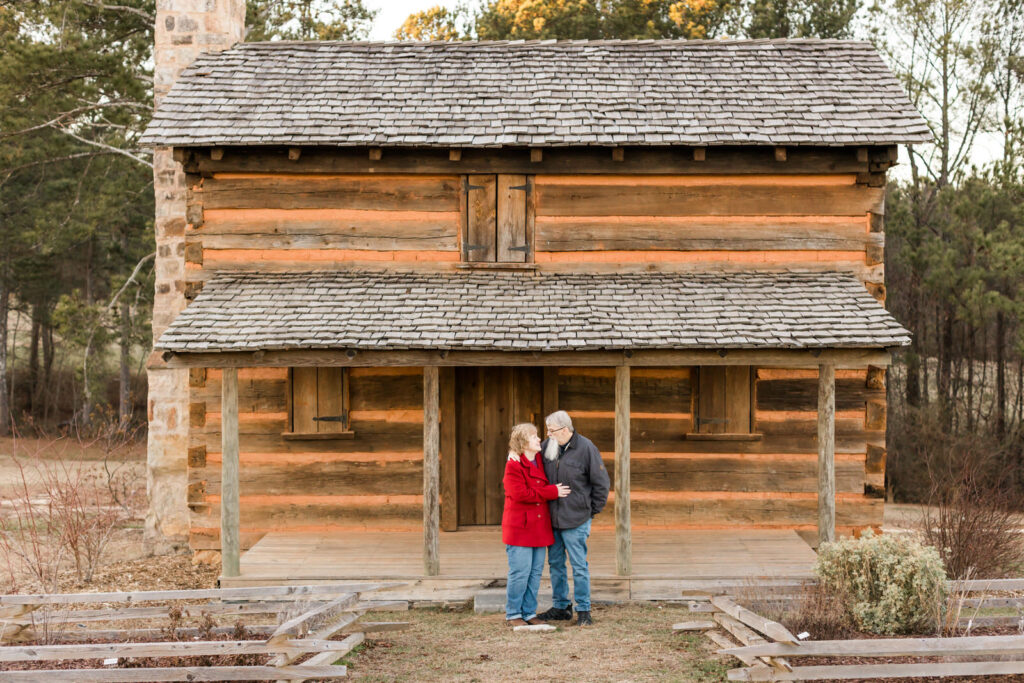 A couple looks at each other while standing in front of a rustic cabin at Cherokee Bluffs Park